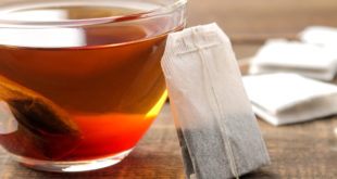 Bustina di tè appoggiata a tazza di vetro contenente tè; sullo sfondo altre bustine