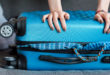 mano femminile che cerca di chiudere una valigia azzurra stracolma; Concept: Viaggio, tossinfezioni