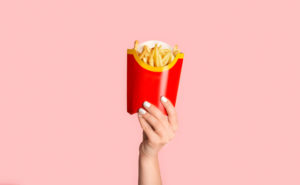 Mano femminile con smalto bianco che mostra patatine fritte da McDonald's in confezione rossa su sfondo rosa