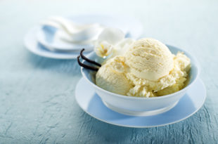 Coppetta di gelato alla vaniglia con bacche di vaniglia, appoggiata su un piattino