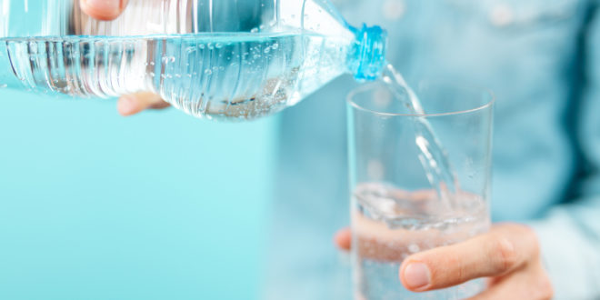 Persona versa acqua minerale da una bottiglia di plastica in un bicchiere