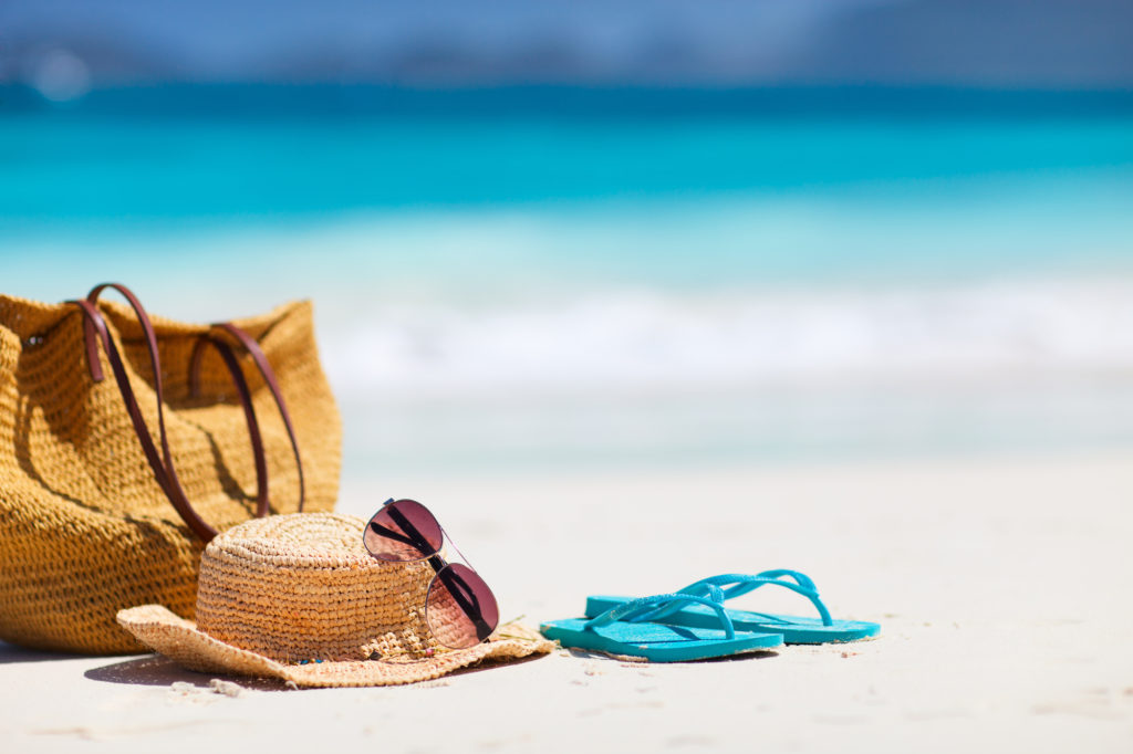 Borsa da spiaggia, occhiali da sole, cappello di paglia e infradito sulla spiaggia 