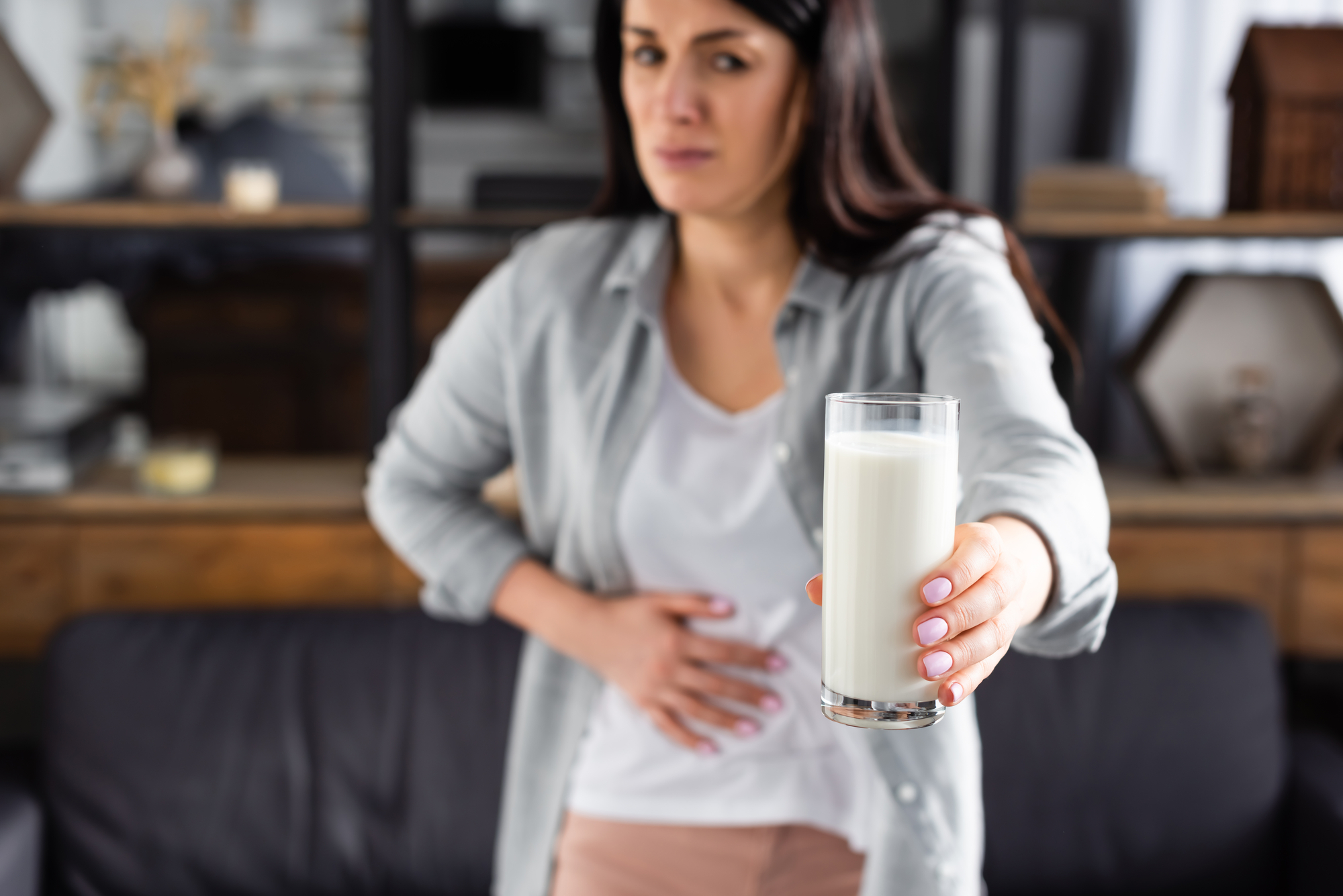 Donna intollerante al lattosio tiene una mano sull'addome e con l'altra regge un bicchiere di latte