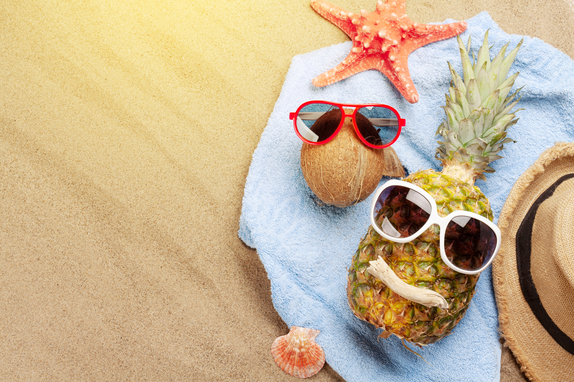 Buona vacanze. rappresentazione divertente frutta esotica, cocco e ananas, con occhiali da sole stella marina e conchiglia su un telo da spiaggia sulla sabbia