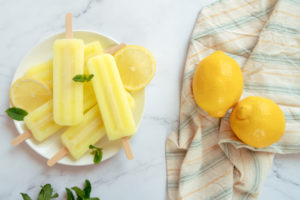 ghiaccioli al limone su piatto bianco con foglioline di menta e fettine di limone come decorazione, e due limoni interi