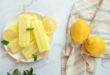 Gelati o ghiaccioli al limone su stecco in un piattino, accanto a due limoni interi su un canovaccio