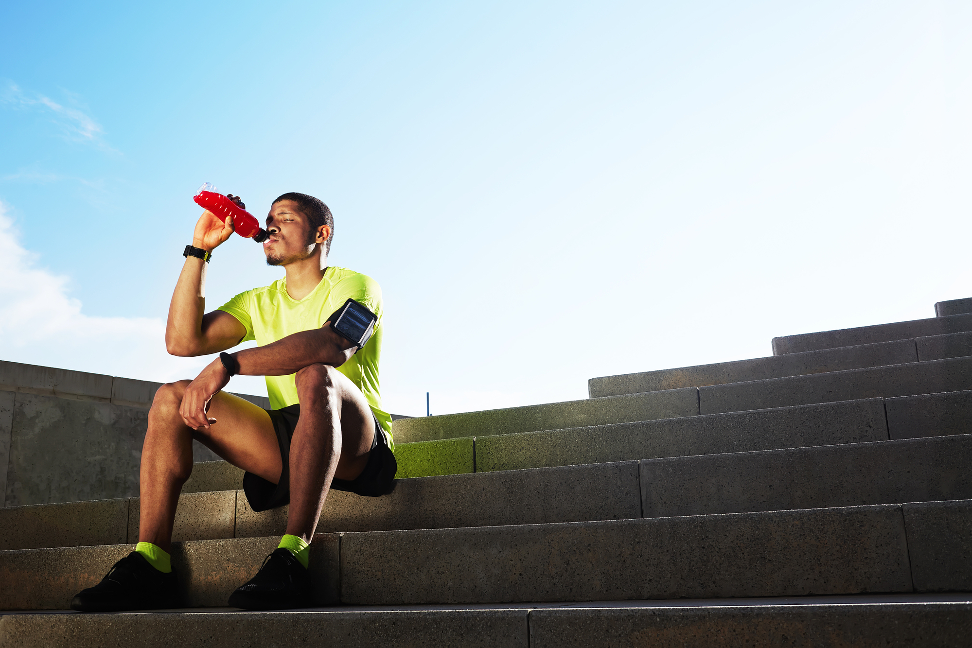 Sportivo beve bevanda isotonica (sport drink) rossa seduto su scalinata