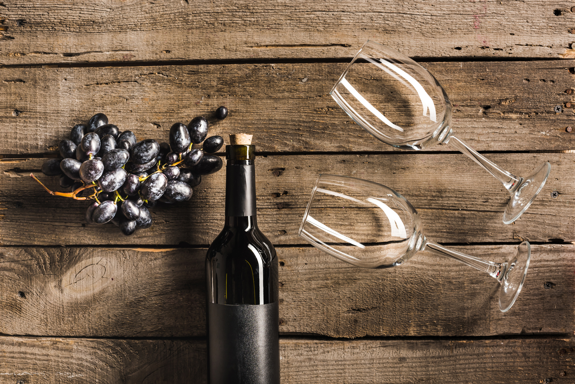 Bottiglia di vino stesa su un tavolo accanto a grappolo di uva nera e due calici