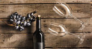 Bottiglia di vino rosso, grappolo di uva nera e due calici distesi su un tavolo di legno