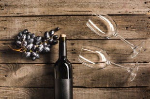 Bottiglia di vino rosso, grappolo di uva nera e due calici distesi su un tavolo di legno