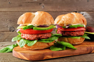 Due panini con burger vegetale, avocado, pomodoro, cipolla e spinacino su un tagliere di legno