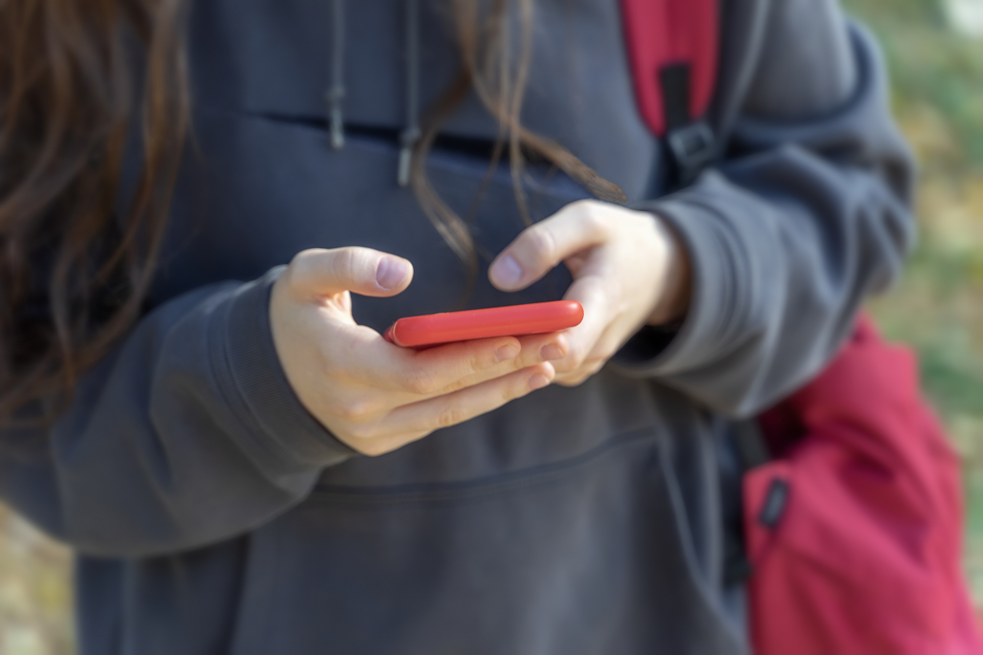 immagine ravvicinata busto di ragazza con mani che tendono smartphone rosso in primo piano