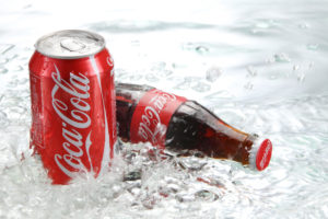 Lattina e bottiglia di vetro di Coca-Cola su acqua