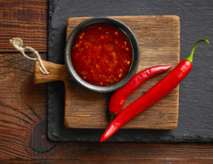 Ciotolina di salsa agrodolce o piccante su un piccolo tagliere di legno con due peperoncini