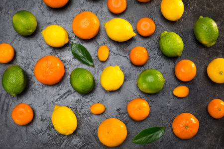 Agrumi misti e alcune foglie su superficie grezza nera: mandarini o clementine, limoni, arance, lime, kumquat
