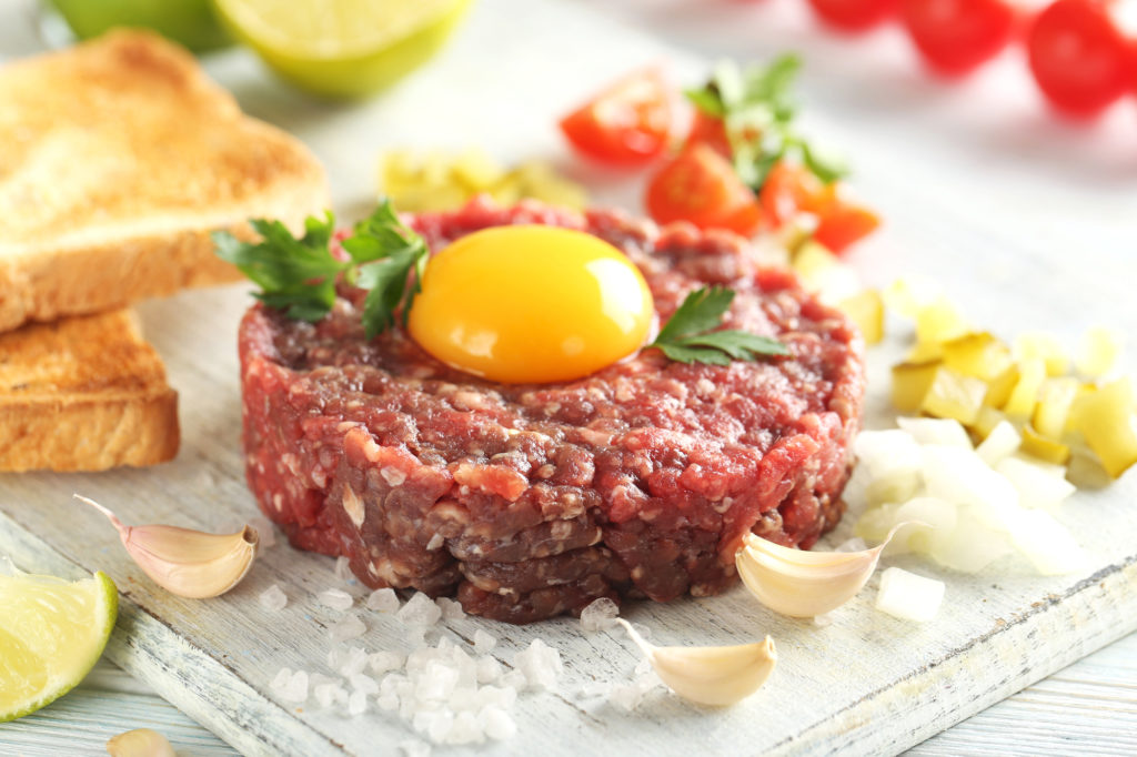 Tartare di manzo con tuorlo d'uovo su un tavolo di legno blu listeria