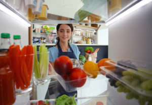 Ritratto di donna in piedi vicino al frigorifero aperto pieno di cibo sano, frutta e verdura. Ritratto di donna.