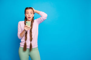 Ritratto di ragazza frustrata impressionata con lunghe trecce ottenere social media blog post commento guardare cellulare smartphone.