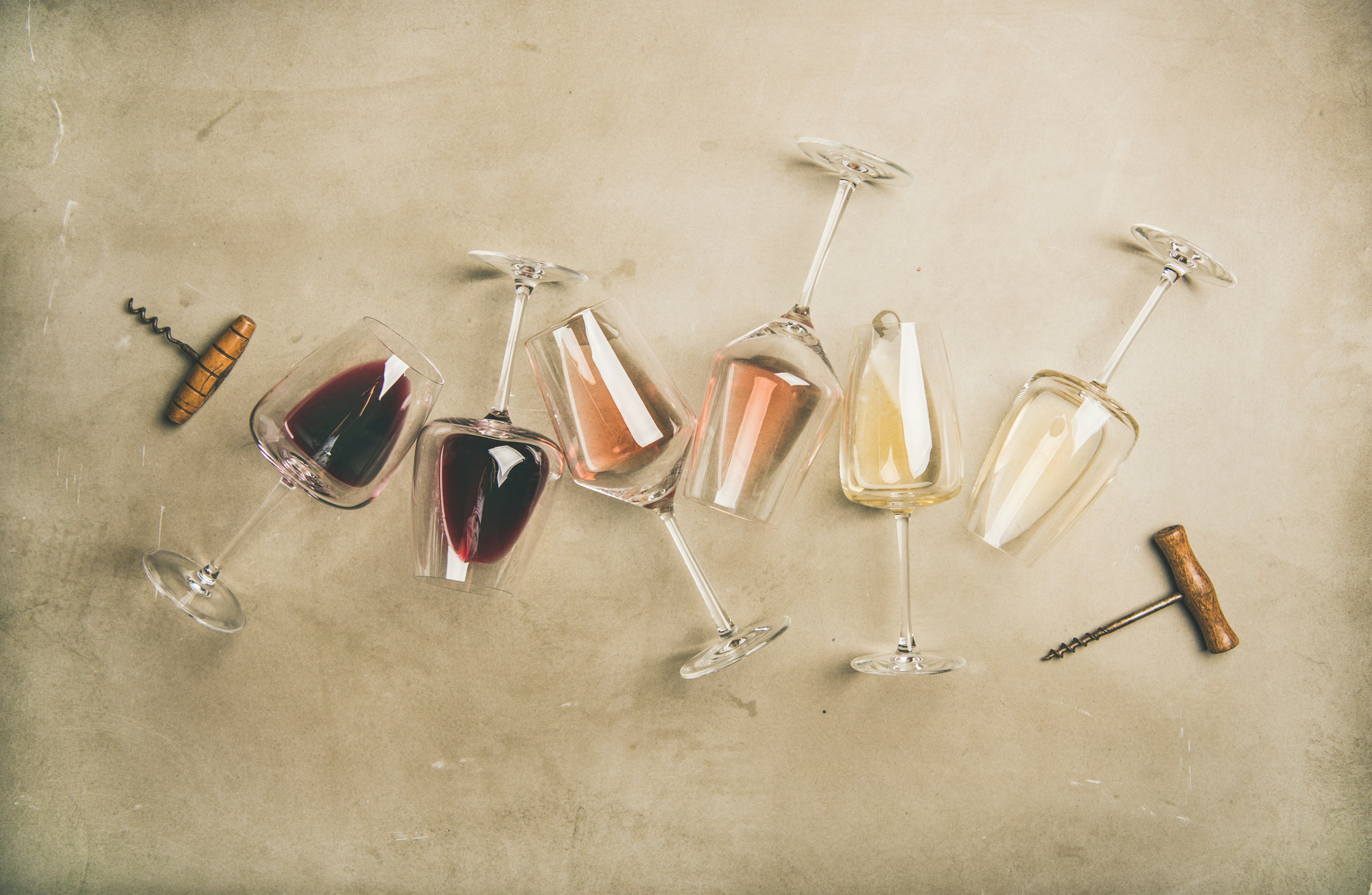 Flat-lay di vino rosso, rosato e bianco in bicchieri e cavatappi su sfondo grigio cemento, vista dall'alto, composizione orizzontale. Wine bar, cantina, concetto di degustazione di vini