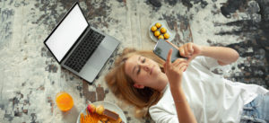 Ragazza teenager sdraiata sul pavimento con laptop e telefono con schermo vuoto che scorre il feed nei social network. Ambiente domestico accogliente