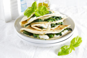 Piadine con spinaci e mozzarella in un piatto con foglie di basilico