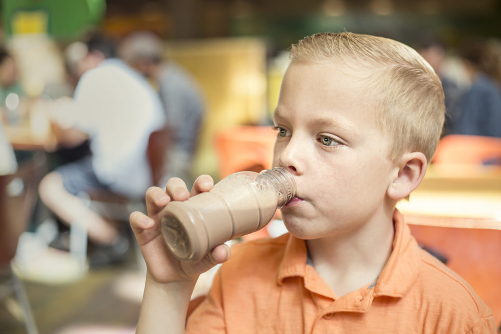 Bambino beve bottiglietta di latte al cioccolato in una mensa scolastica