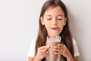 Bambina si lecca le labbra mentre tiene in mano bicchiere di latte al cioccolato