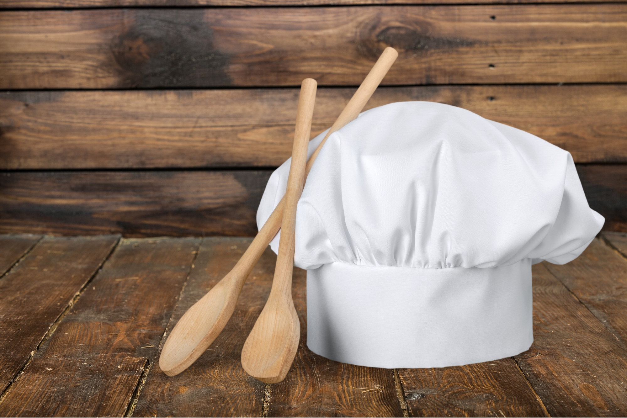 Cappello da chef con due mestoli di legno su superficie di legno scuro
