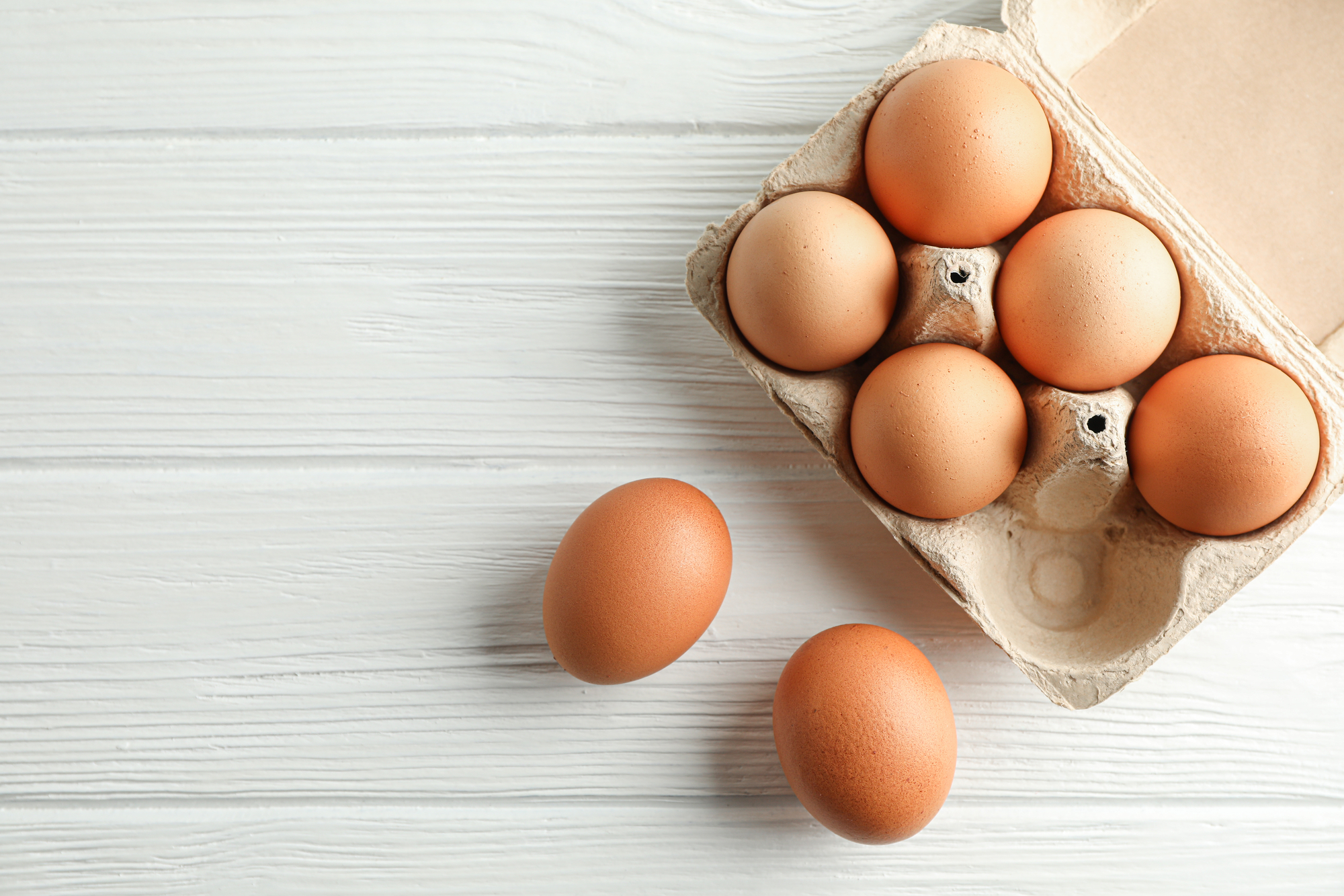 5 Uova di gallina in cartone e due uova su tavolo bianco