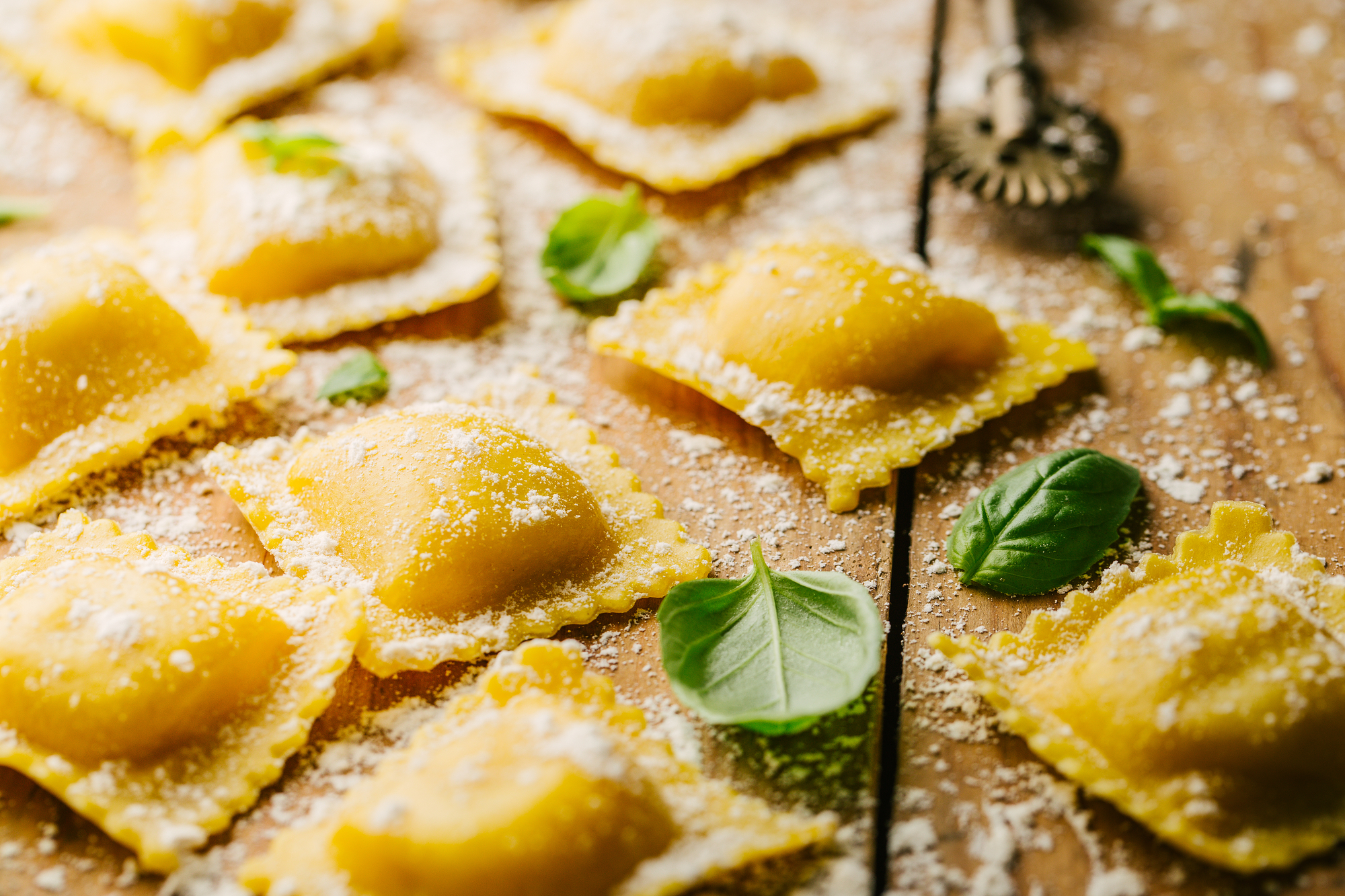 Ravioli crudi su un tavolo di legno con farina e foglie di basilico