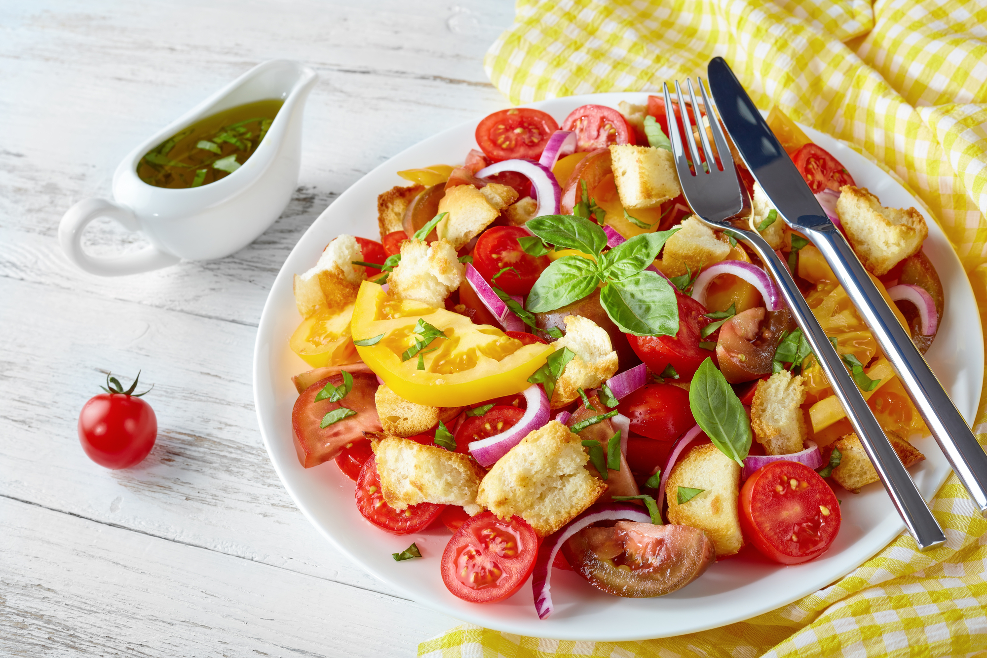 Un piatto di panzanella a base di pomodori, cipolla e crostini di pane, con basilico e salsiera con olio. dieta vegana 