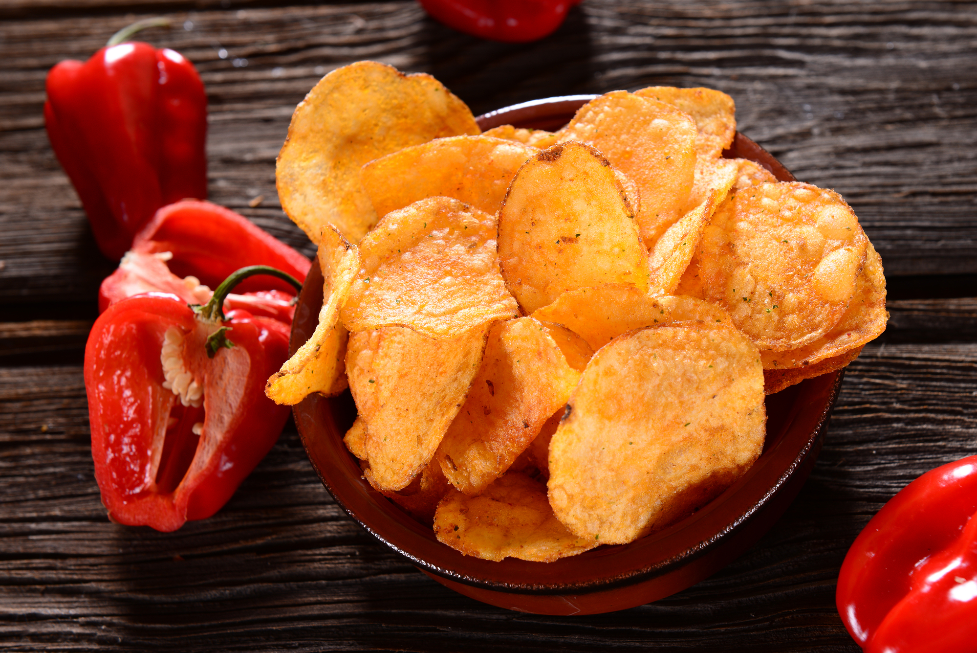 Ciotola di patatine chips alla paprika, circondata da peperoni rossi