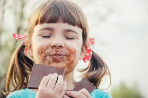 Bambina con faccia sporca di cioccolato mangia una tavoletta di cioccolato