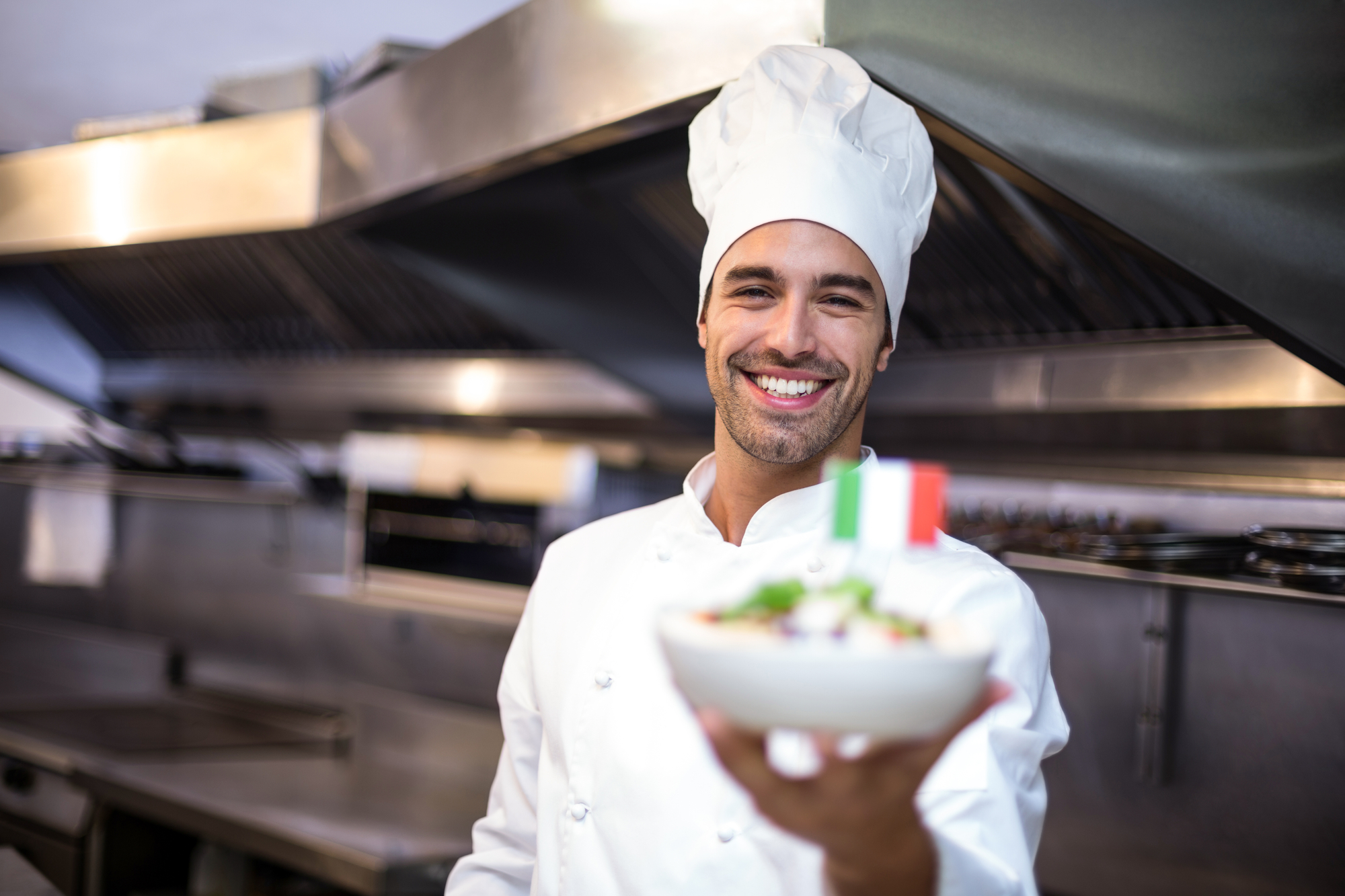 Chef o cuoco nella cucina di un ristorante italiano tiene in mano piatto di pasta con bandiera italiana