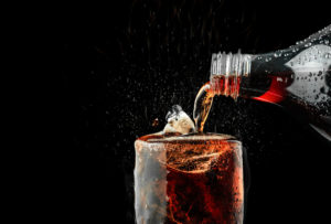 Bevanda zuccherata o con edulcoranti tipo cola versata da una bottiglia in un bicchiere con ghiaccio