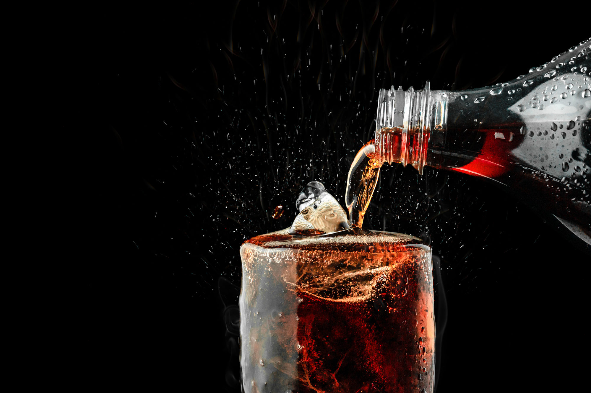 Bevanda zuccherata o con edulcoranti tipo cola versata da una bottiglia in un bicchiere con ghiaccio
