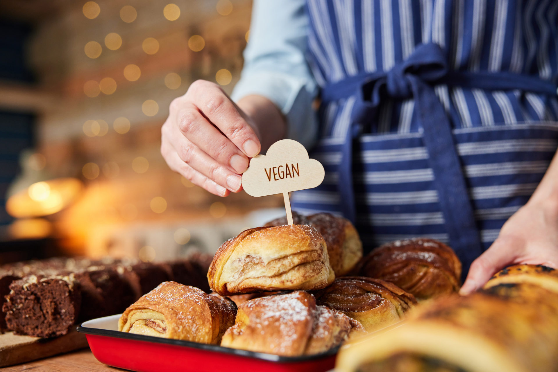 Pasticcere o commesso mette cartellino con scritta vegan su cinnamon buns vegani; concept: vegano, plant-based