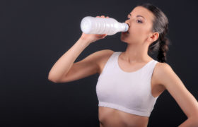 Donna in tenuta sportiva che beve latte o yogurt dalla bottiglia; concept: alimenti proteici, proteine