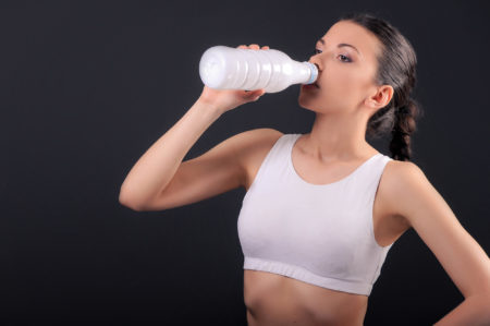 Donna in tenuta sportiva che beve latte o yogurt dalla bottiglia; concept: alimenti proteici, proteine