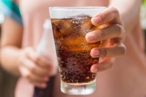 Donna tiene in mano un bicchiere con una bevanda zuccherata tipo Coca-Cola e ghiaccio; concept; bevande zuccherate, bibite