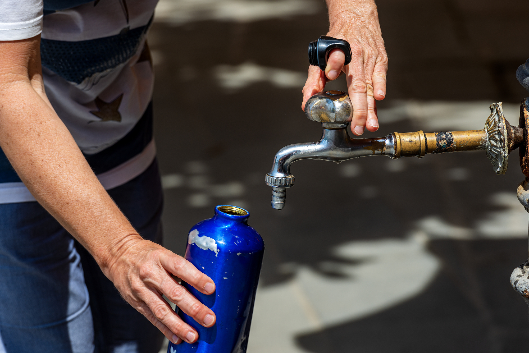 Primo piano della mano di una donna mentre riempie una borraccia con l'acqua del rubinetto in una calda giornata estiva. Italia, Europa PFAS