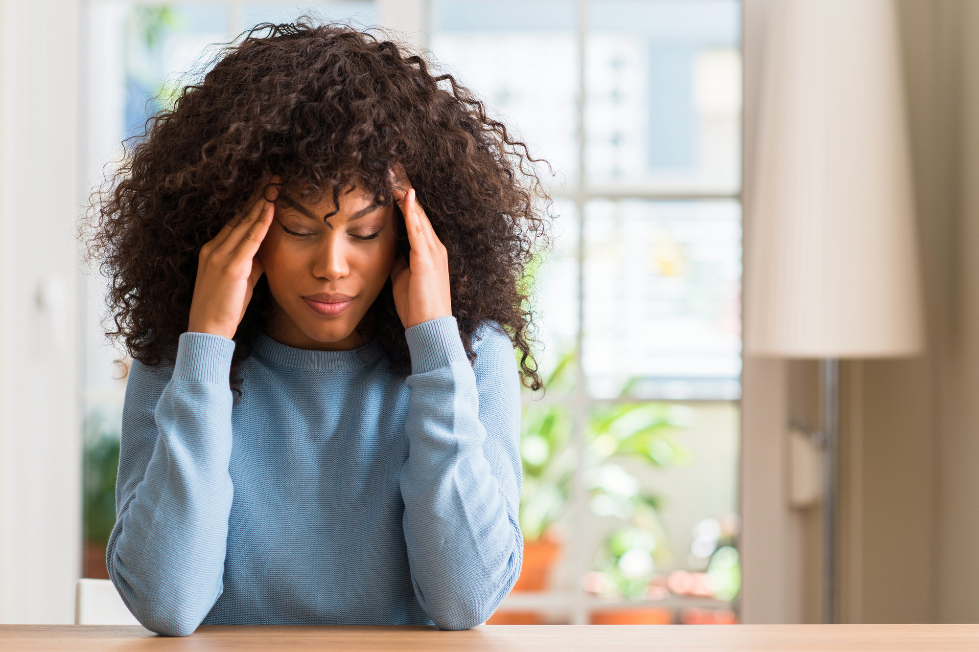 Donna afroamericana a casa con la mano sulla testa per il dolore alla testa dovuto allo stress. Soffre di emicrania. mal di testa