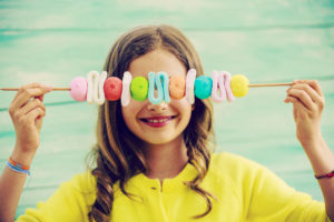 Bambina sorridente tiene davanti agli occhi spiedino di marshmallow e caramelle; concept: dolci, zucchero