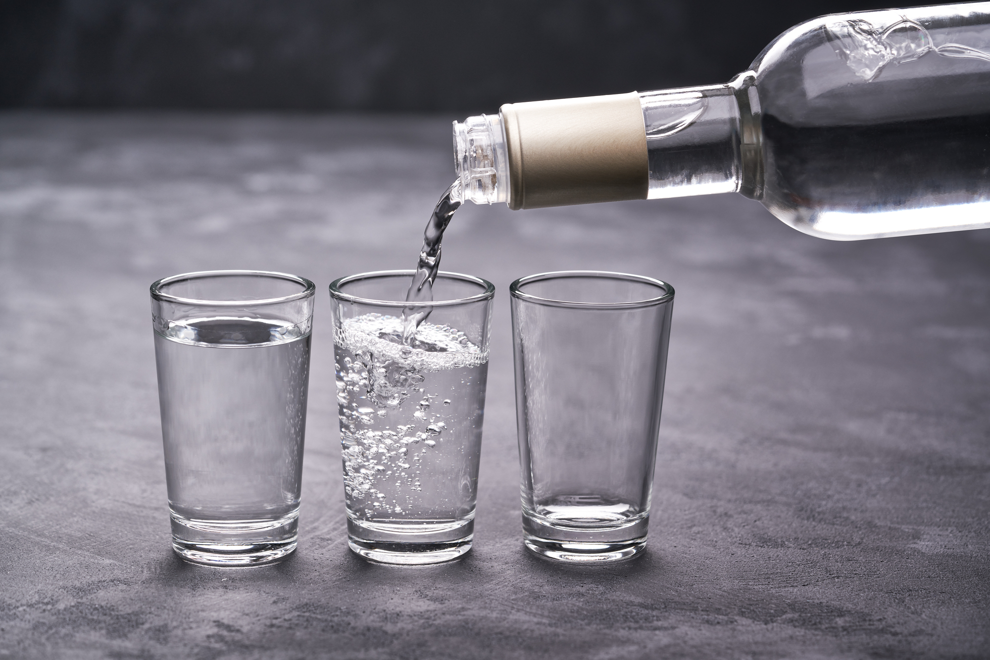 Vodka versata da una bottiglia in bicchierini da shot; concept: alcol