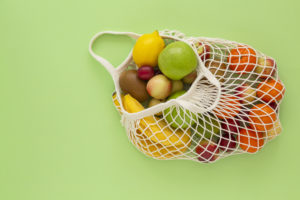 Frutta assortita in una borsa riutilizzabile a rete su sfondo verde