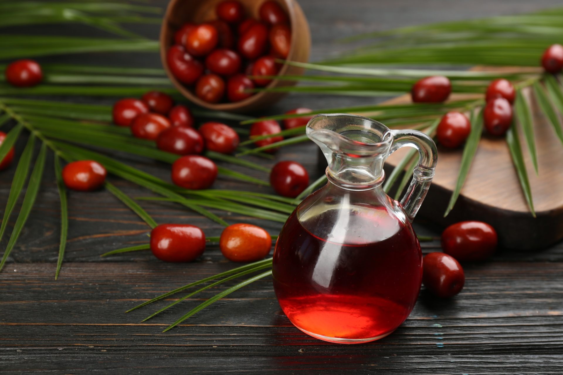 Olio di palma in una brocca di vetro, foglie e frutti tropicali su un tavolo di legno