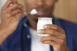 Uomo mangia uno yogurt bianco; concept: proteine, latticini