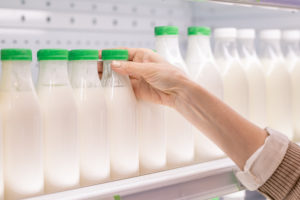 Mano femminile prende bottiglia di latte fresco dal banco frigo di un supermercato