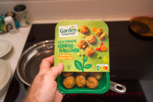 Persona tiene confezione di polpette vegetali Garden Gourmet con Nutri-Score A sopra piastra a induzione