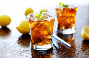 Due bicchieri di té freddo al limone con ghiaccio e foglie di menta su un tavolo con limoni